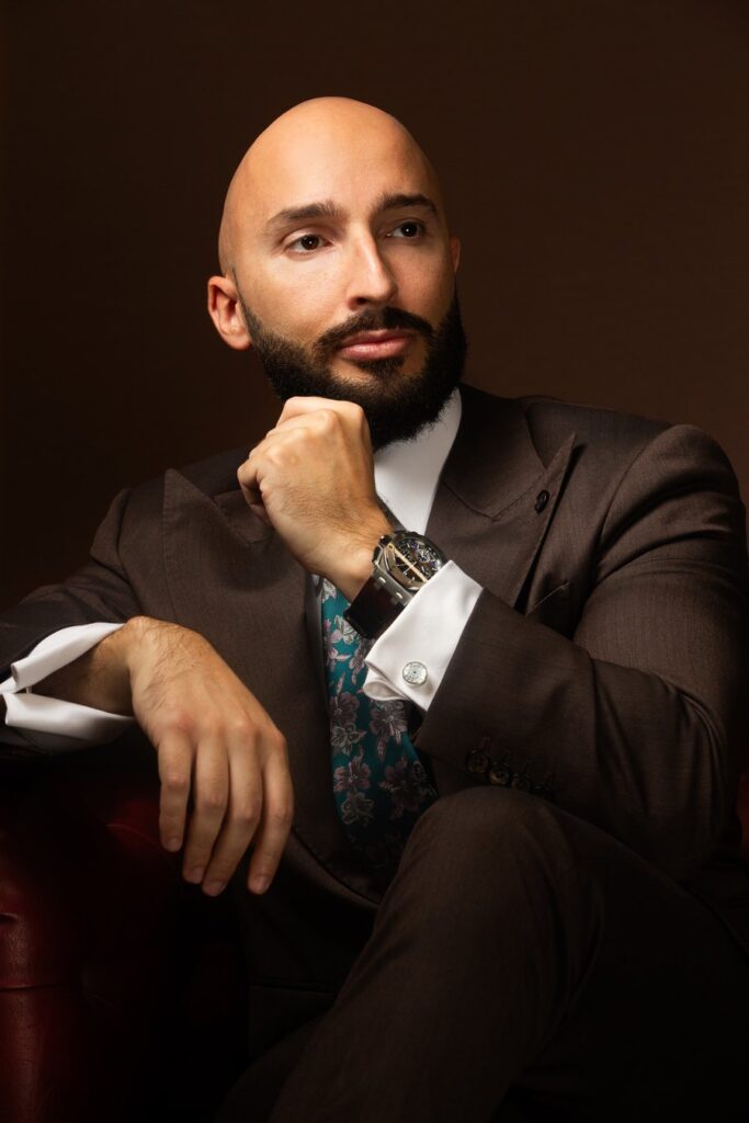 Daniele Pescara seduto, la mano sotto il mento, ritratto in studio su fondo bruno