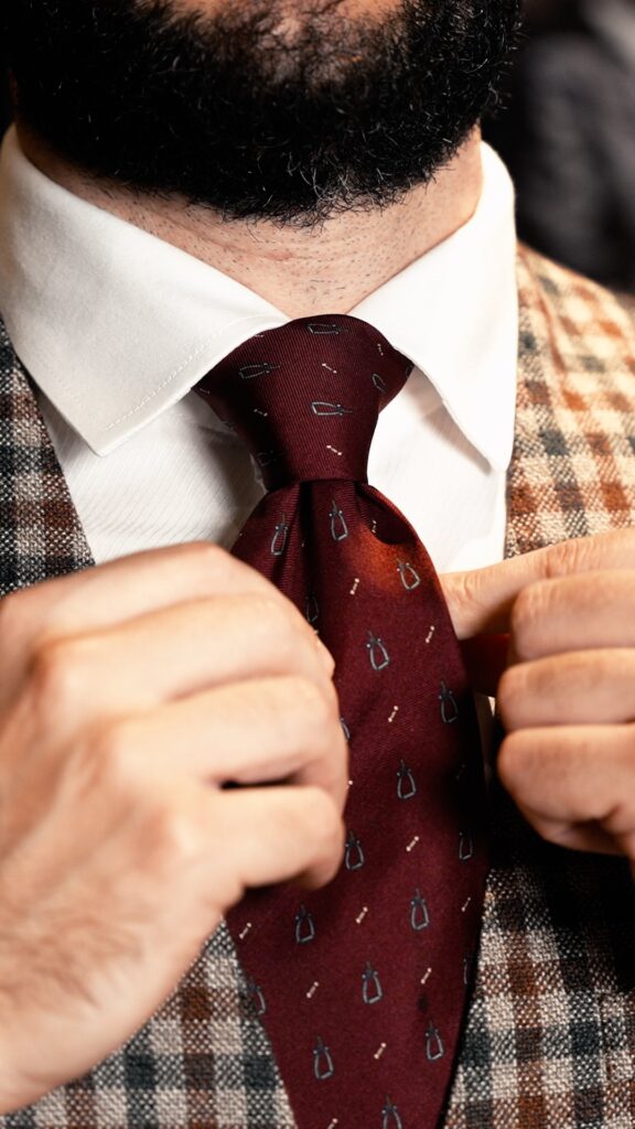 Primo piano: due mani stringono il nodo di una cravatta bordeaux sopra una camicia bianca